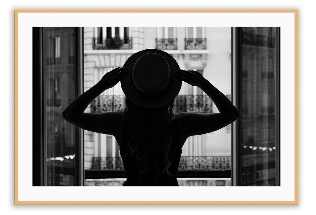 A vintage fashion wall art with a cinematic scene of a parisian woman wearing a hat looking out to the city on the balcony. 