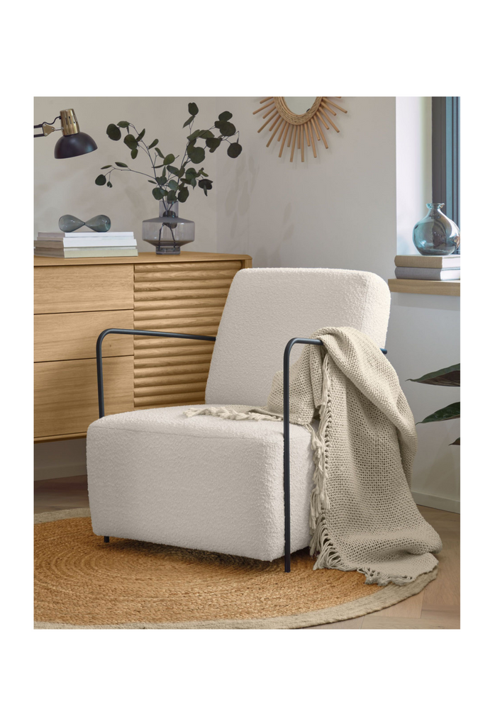 White boucle armchair with black metal frame and wire arm rests on a white background