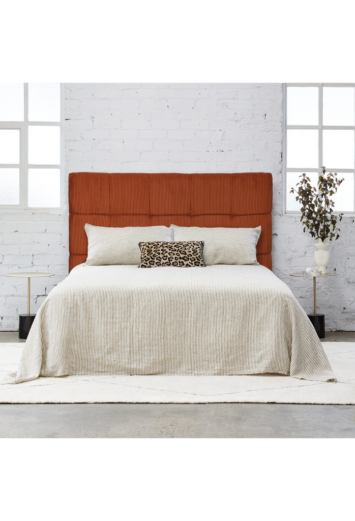 Modern padded bedhead fully upholstered in a soft burnt orange cord fabric with square shaped stiching details on a white background