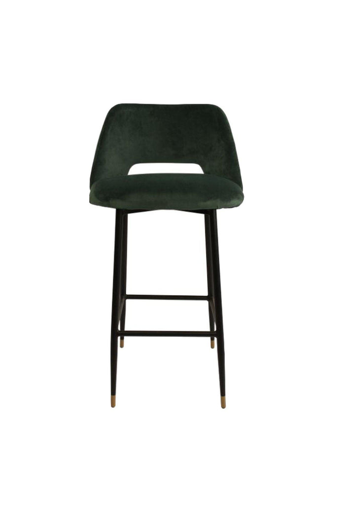 Black bar stool with seat and backrest upholstered in dark green velvet and black metal frame feauring a foot rest on a white background