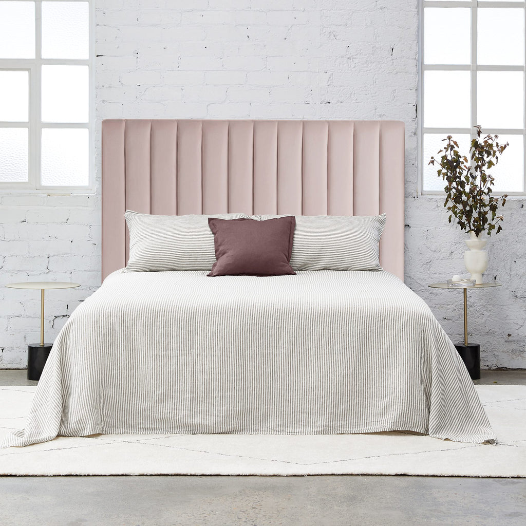 Free standing rectangular bedhead with padded panels fully upholstered in blush pink velvet on a white background