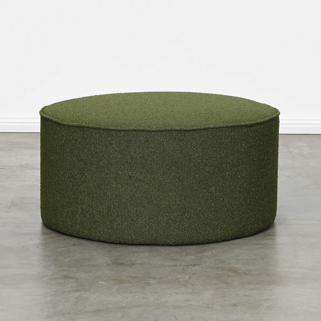 Large Round Ottoman Fully Upholstered in Textured Dark Green Fabric with Piped Edges on White Background