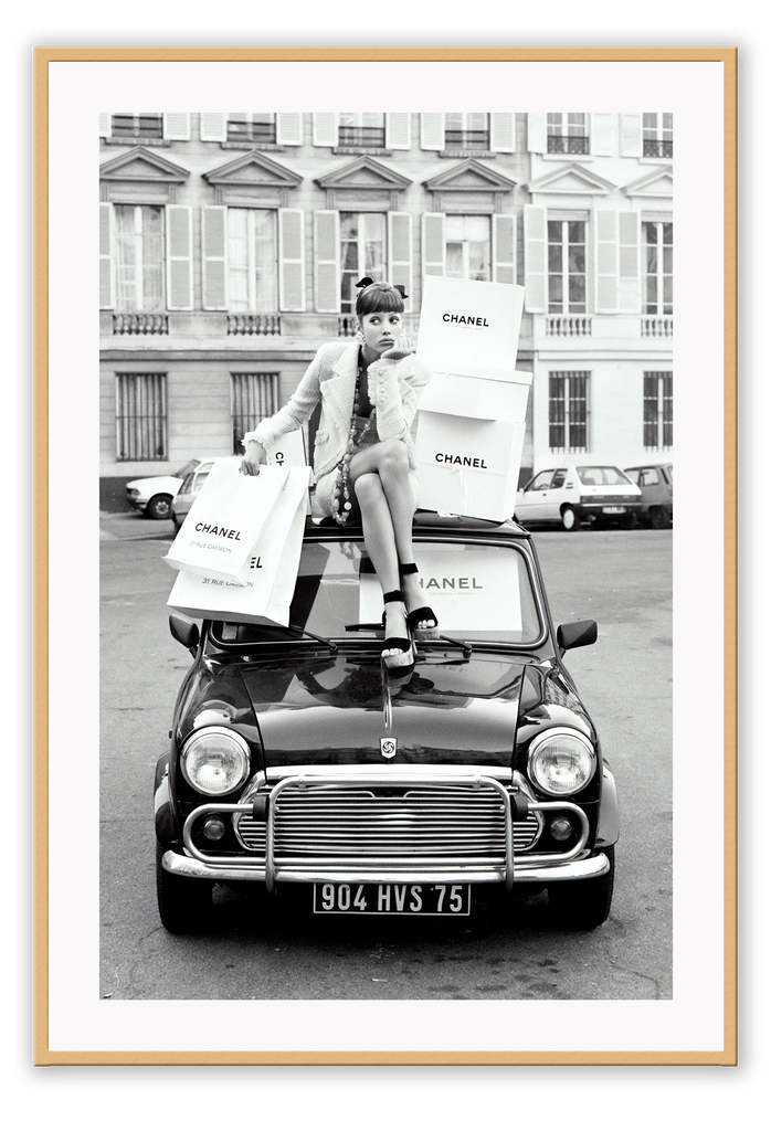 A black and white vintage fashion wall art with a lady holding Chanel shopping bags riding on vintage car Fiat in European city. 