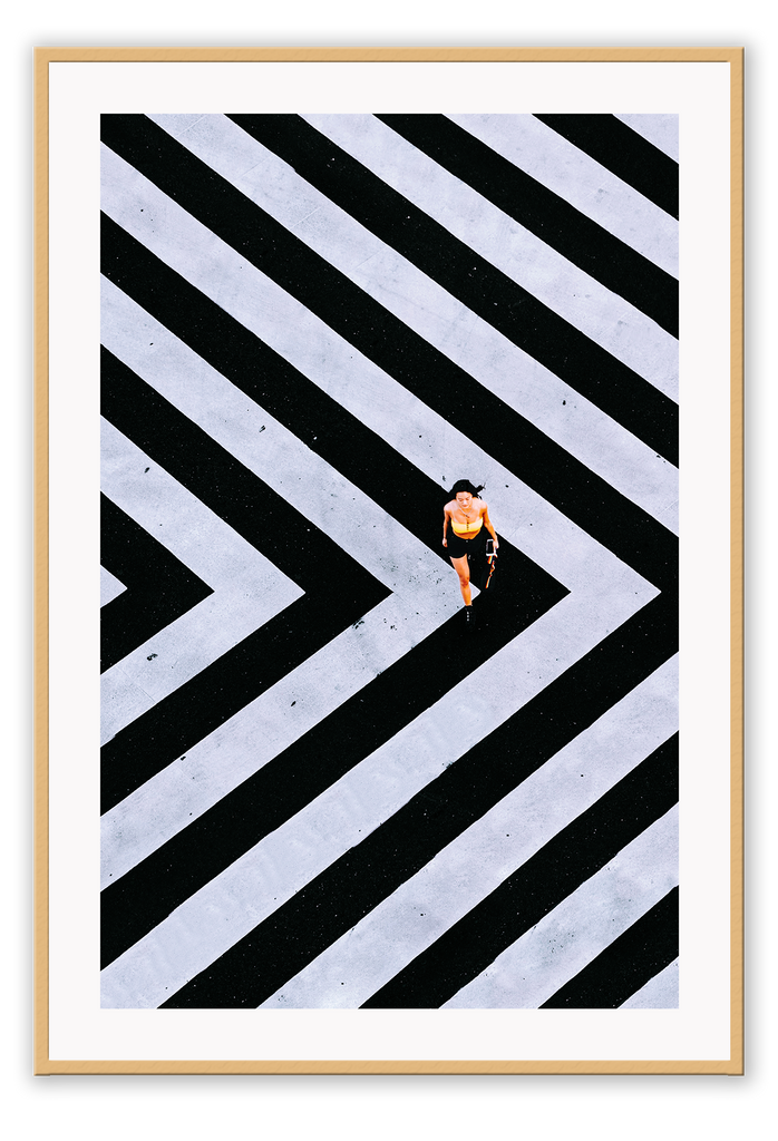 An urban wall art with an aerial view of a lady walking on black and white street crossing stripes