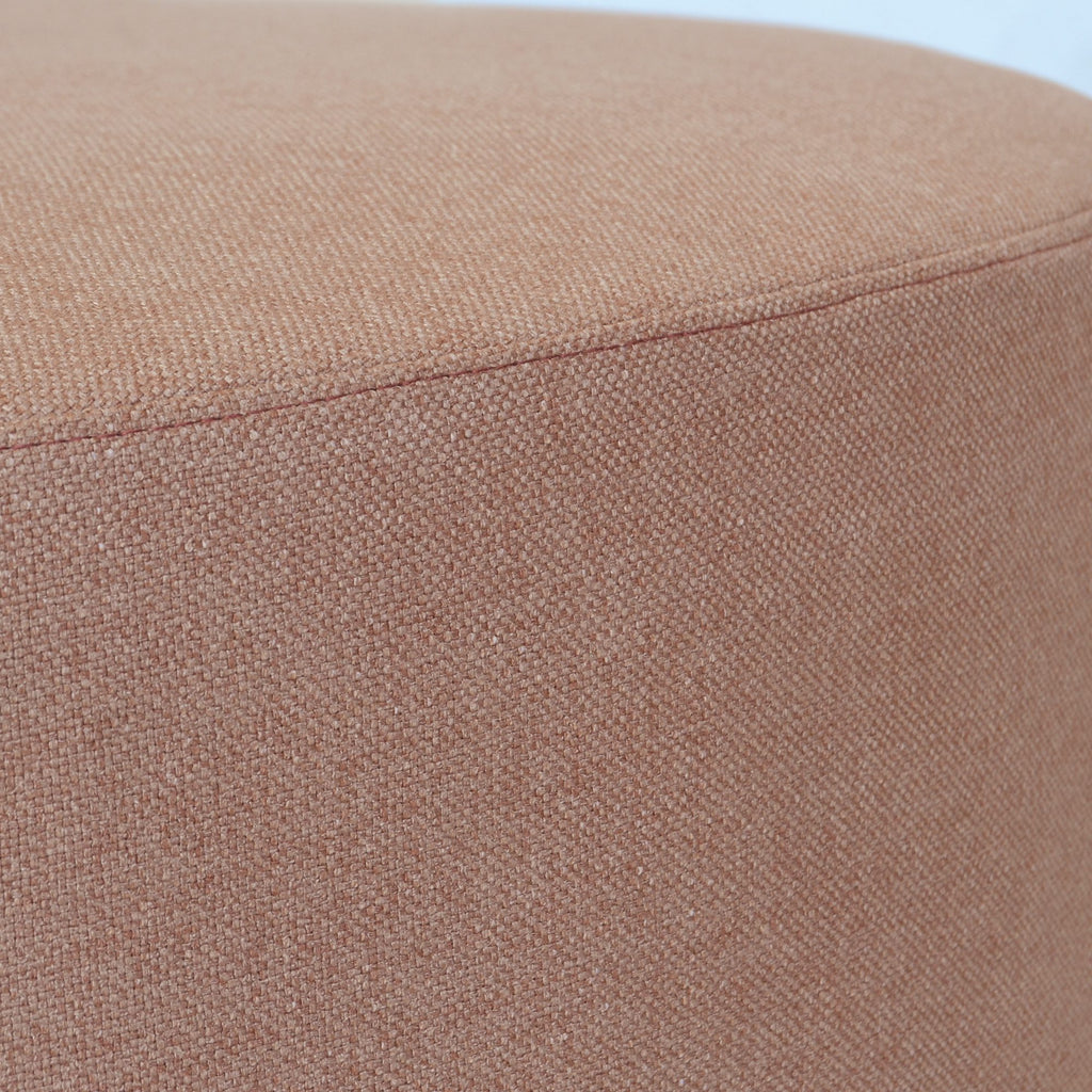 Large round ottoman fully upholstered in an orange rust coloured textured fabric with a black powder-coated metal base