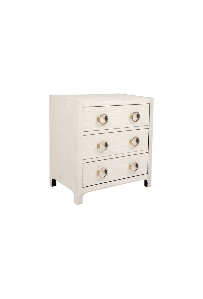 Sharp shaped bedside table fully upholstered in off-white natural linen with three drawers featuring round brass handles on a white background