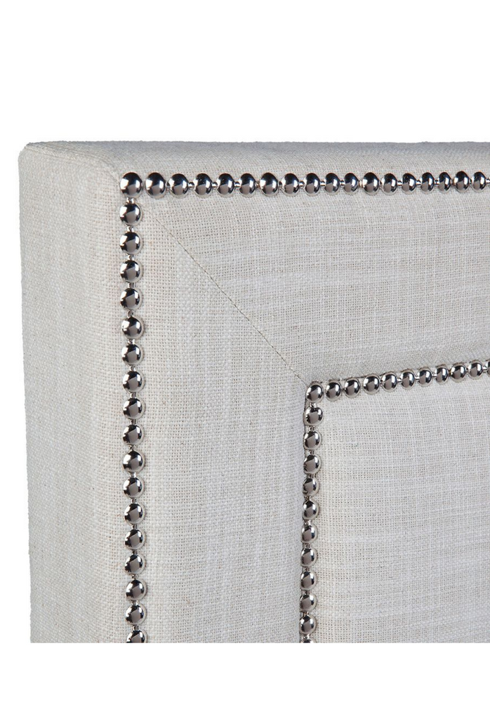 Free standing bedhead fully upholstered in natural linen with sharp edges and studded detailing on a white background