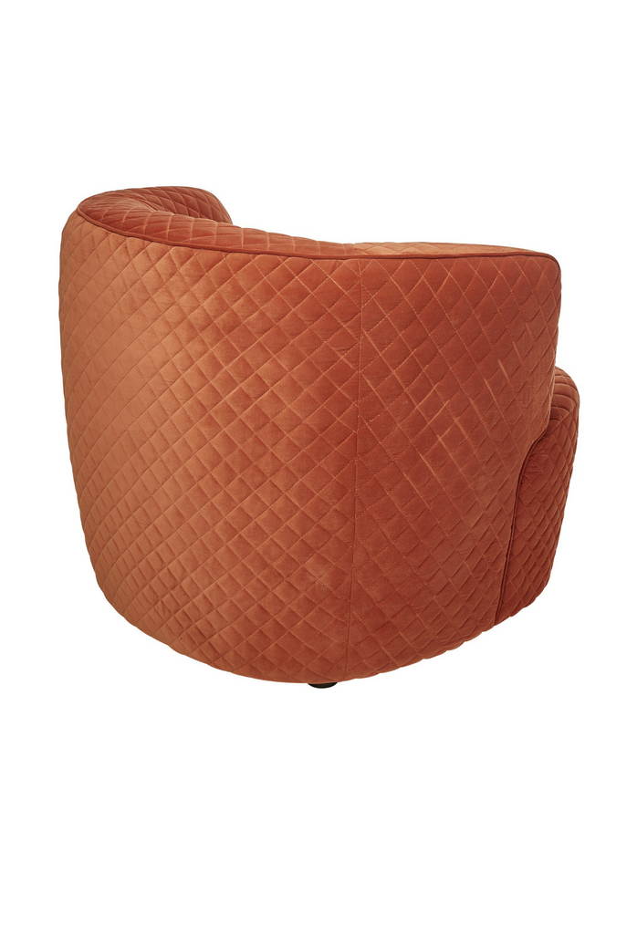 Chunky quilted tub-style armchair fully upholstered in pink orange velvet with curved back and arm rest on a white background