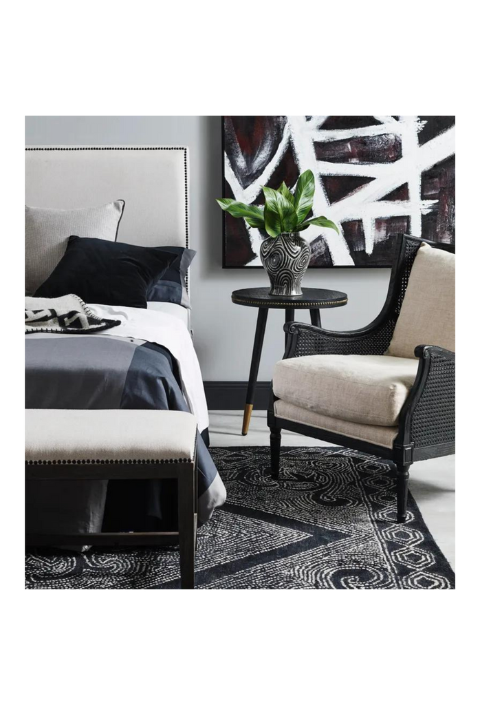 Black wing-back style occasional chair with rattan arm and back rest and timber legs featuring hand-carved detailing and natural linen cushion