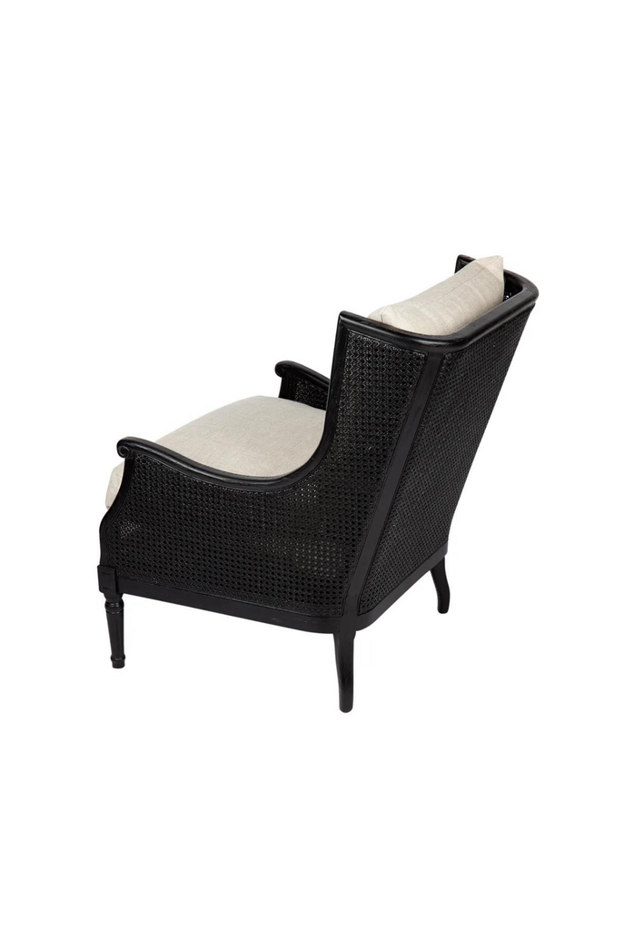 Black wing-back style occasional chair with rattan arm and back rest and timber legs featuring hand-carved detailing and natural linen cushion