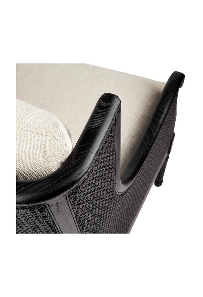 Black wing-back style occasional chair with rattan arm and back rest and timber legs featuring hand-carved detailing and natural linen cushion