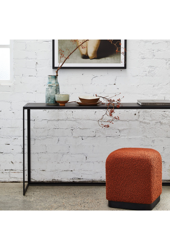 Minimalistic cubic ottoman with soft edges fully upholstered in brick rust boucle on a matte black metal base