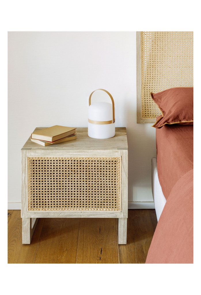 Cubic bedside table with light timber veneer finish and braided rattan front which opens to one side on geometric timber legs