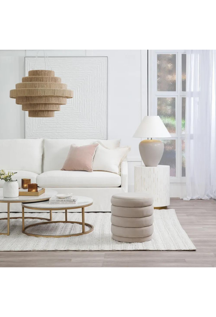 Petite round ottoman with four padded layers and an upholstered base all upholstered in nude velvet on white background