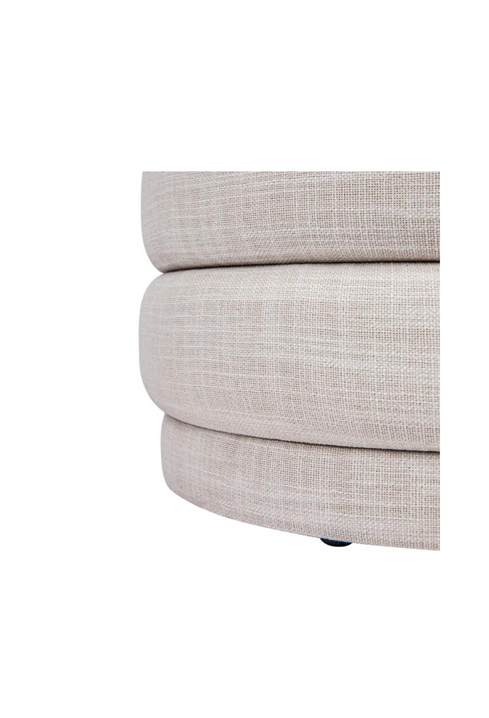 Petite round ottoman with four padded layers and an upholstered base all upholstered in off-white linen on white background