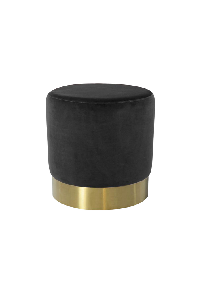 Petite round ottoman fully upholstered in black velvet with a brushed gold base on a white background