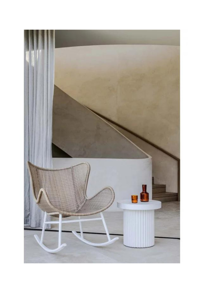 Modern wingback style rocking chair with beige woven ecolene resin seat and white metal base on white background