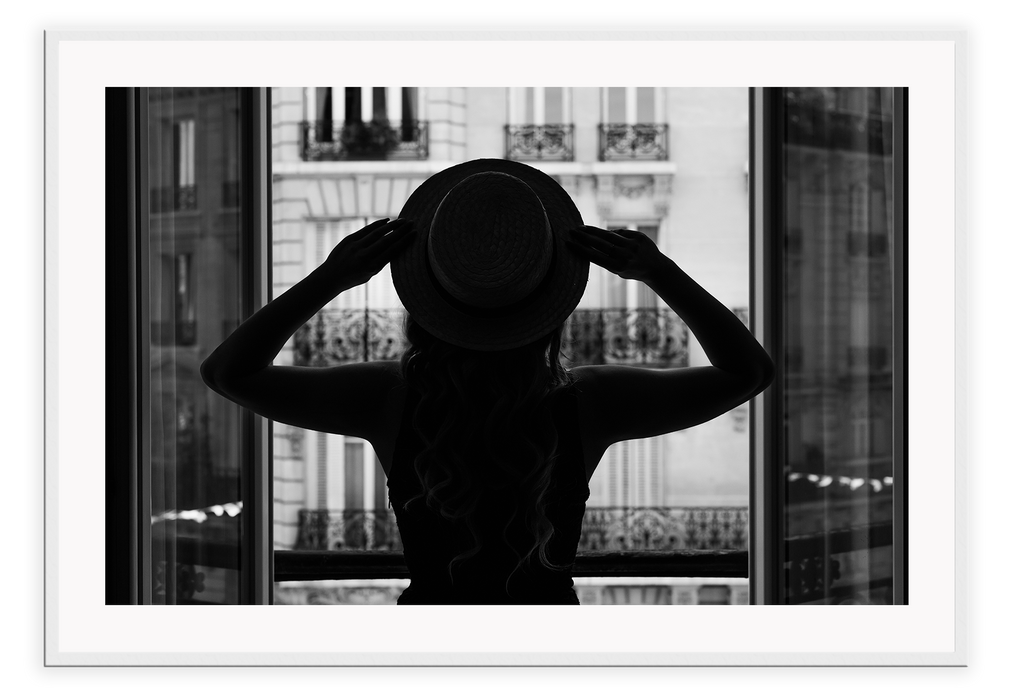 A vintage fashion wall art with a cinematic scene of a parisian woman wearing a hat looking out to the city on the balcony. 