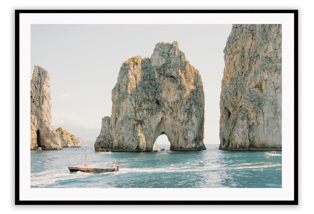 Coastal style photography beach landscape print with large grey rocks and a boat in the ocean.