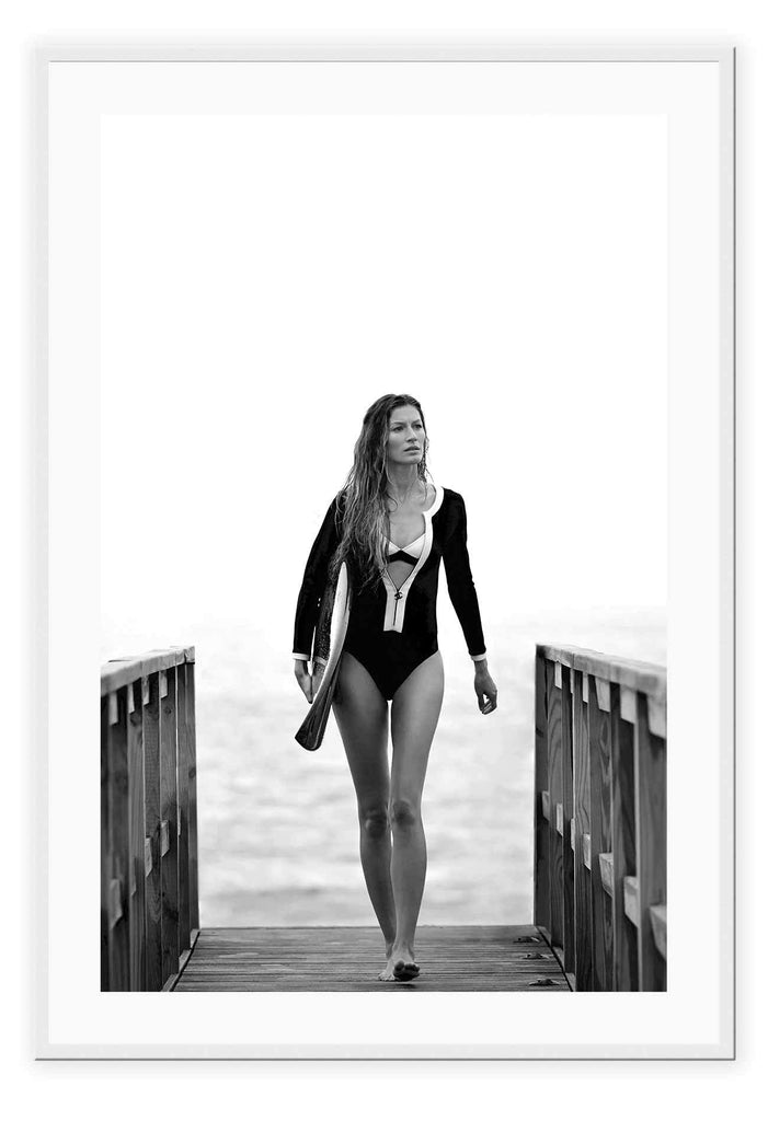 A black and white fashion wall art with Brazilian model Gisele Bundchen holding a surf board walking on timber wharf.