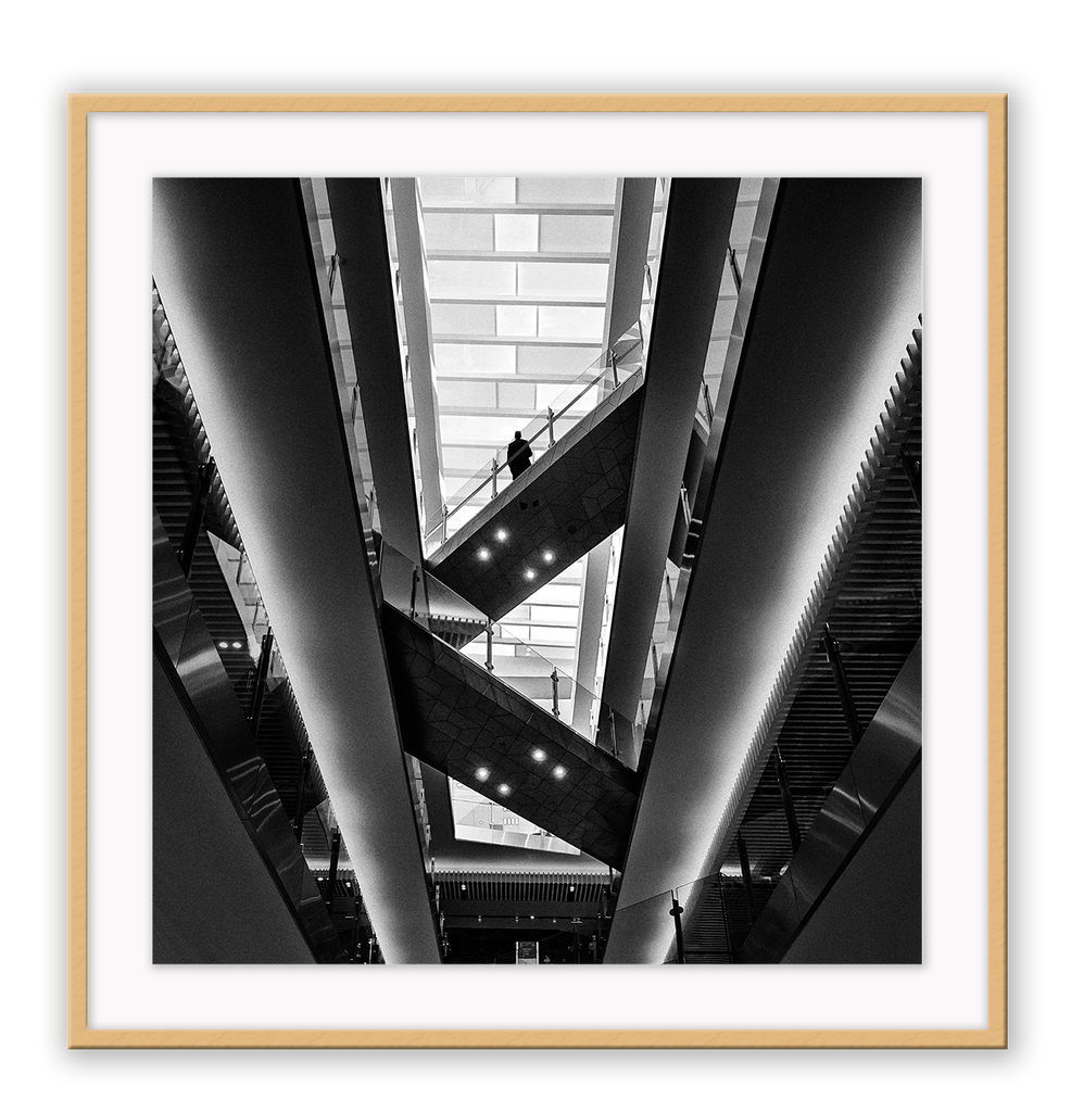 Photography print in black and white with man standing on accending escalator.