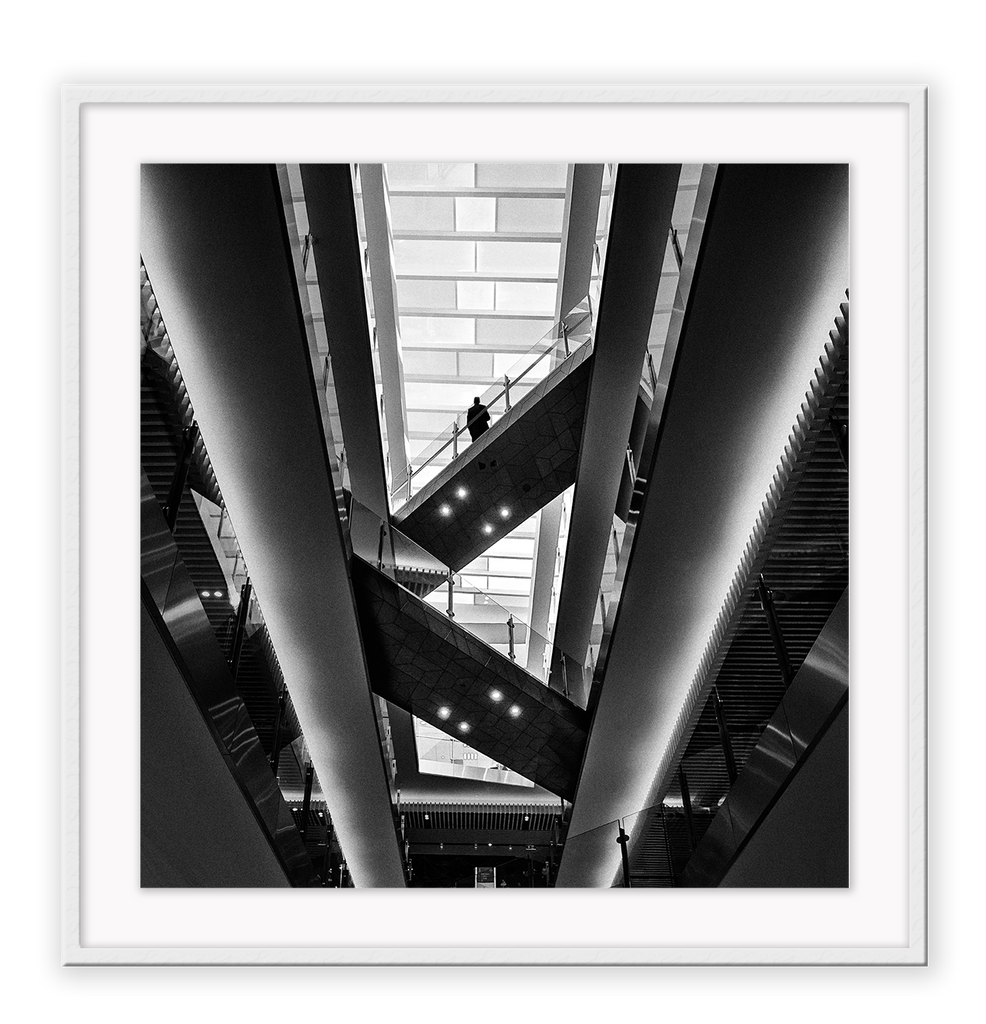 Photography print in black and white with man standing on accending escalator.