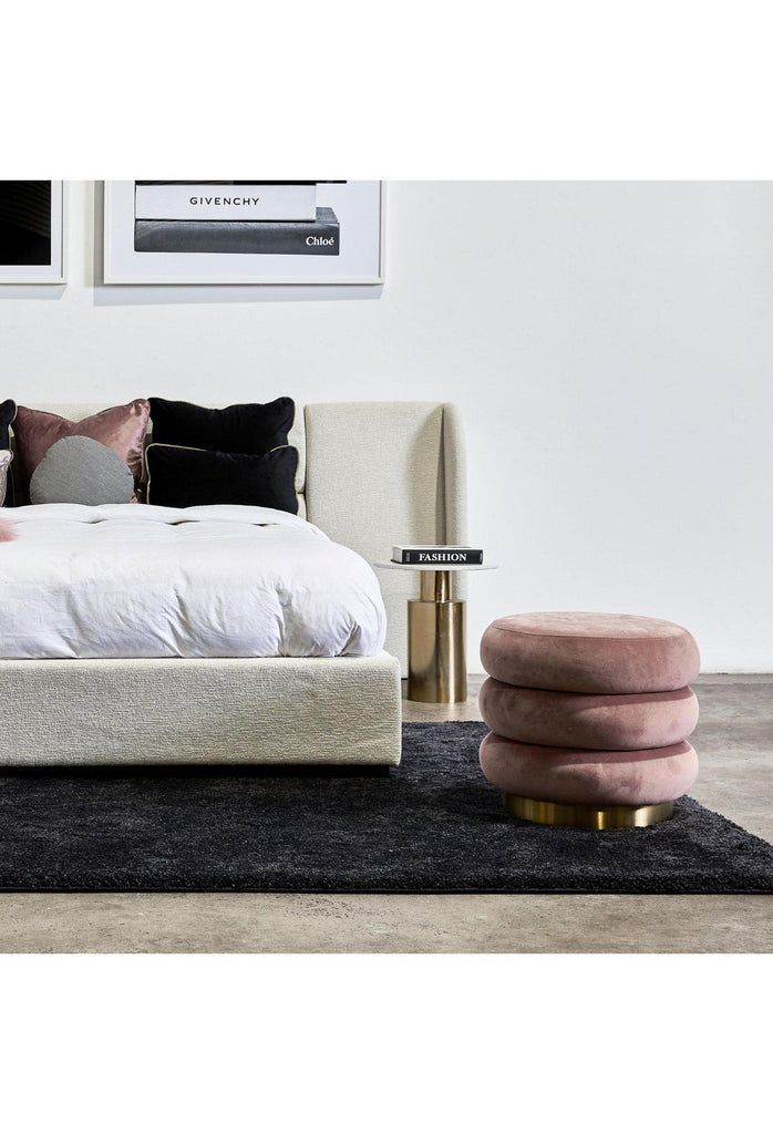 Round ottoman with three layers creating ribbed shape upholstered in blush pink velvet with brushed gold base