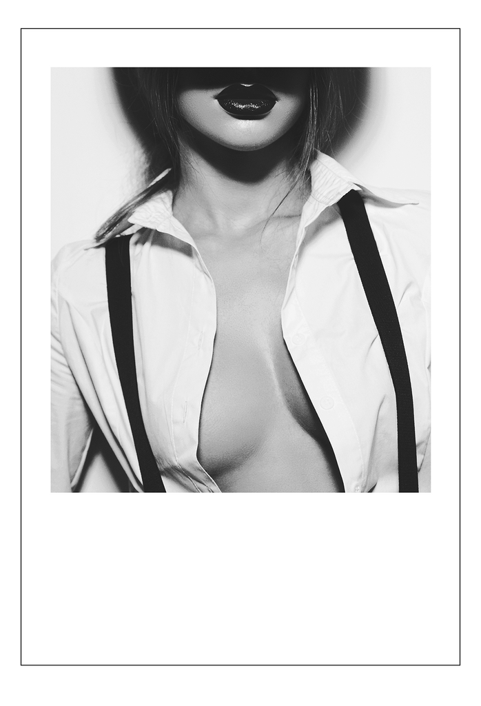 A black and white fashion wall art with a sexy female model wearing white button up and suspenders with breasts exposed. 