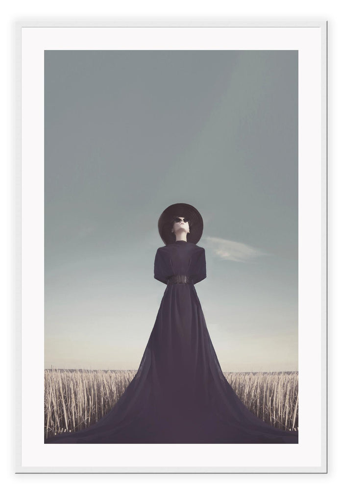 Photography print with woman in black dress and hat looking at sky in field washed natural colours